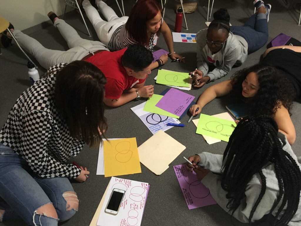 participants circle around, sitting and lying down on the floor while they work together.